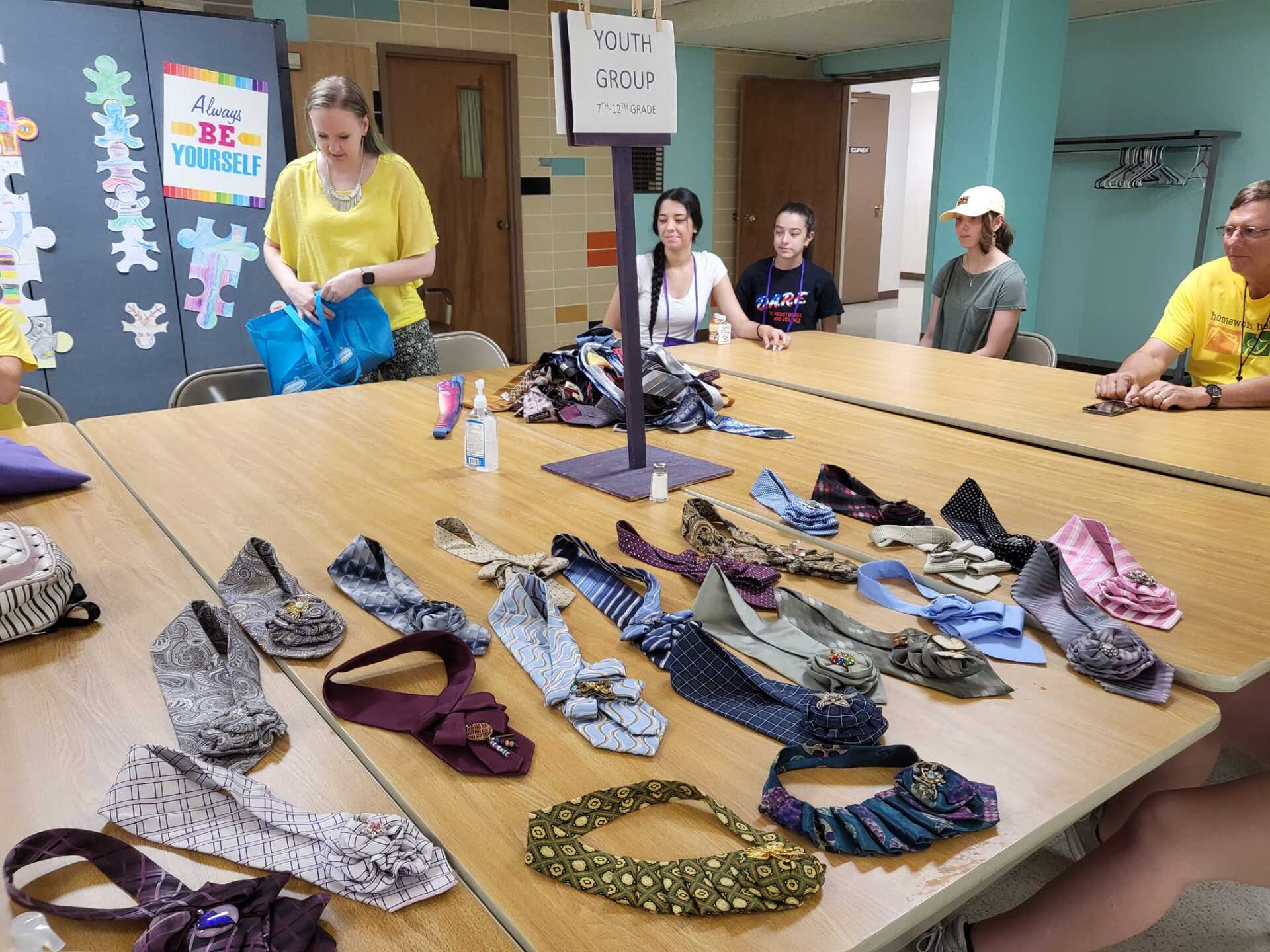 People around a table with handmade shoes made from neckties.