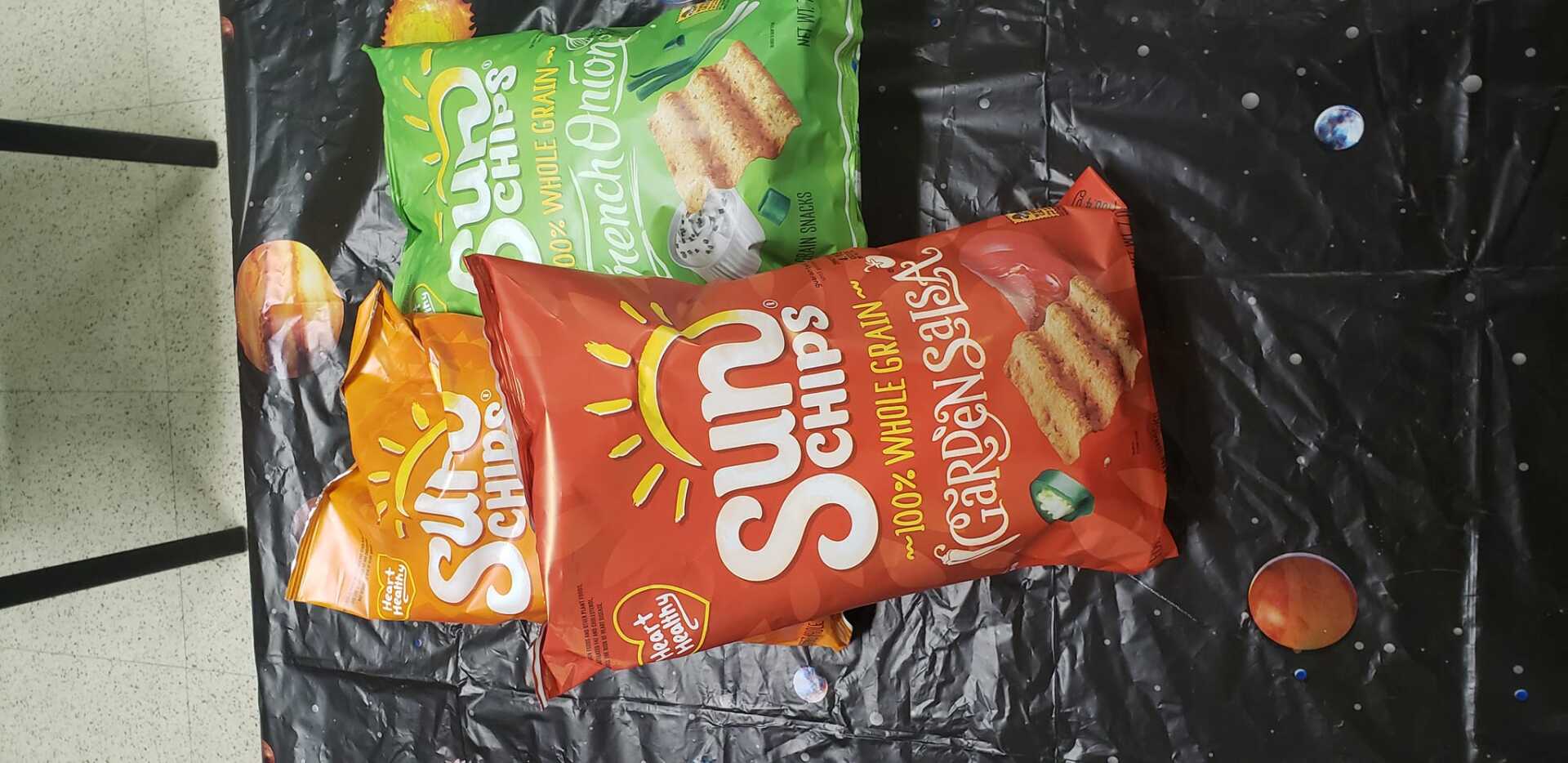 Three bags of Sun Chips on black surface with small colored spheres.