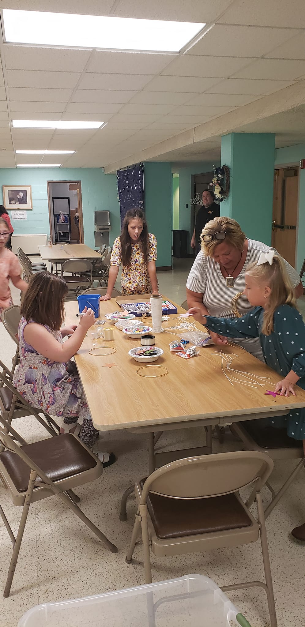 People around a table with scattered items, indoors.