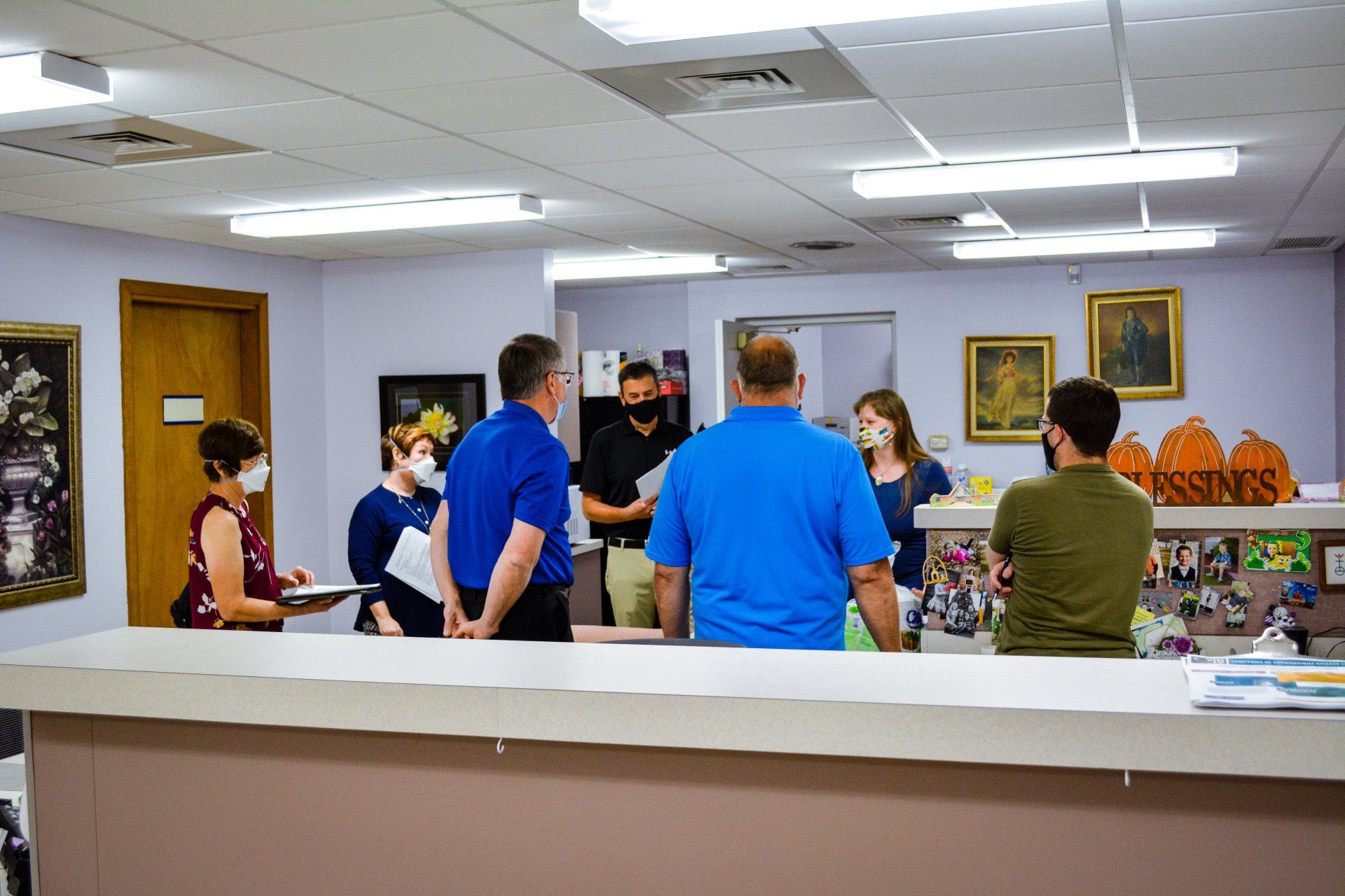 People in office setting, some wearing masks, gathered around a counter.