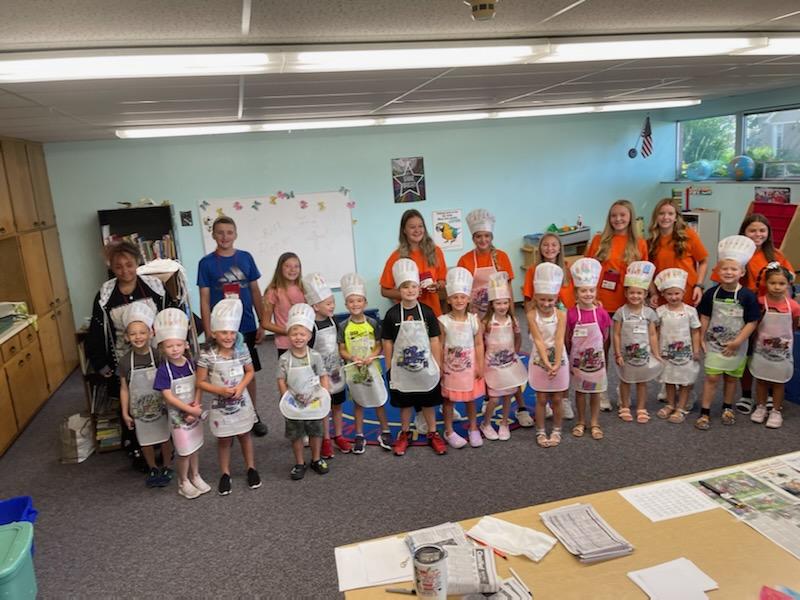 Children in chef hats and aprons stand together in a classroom.