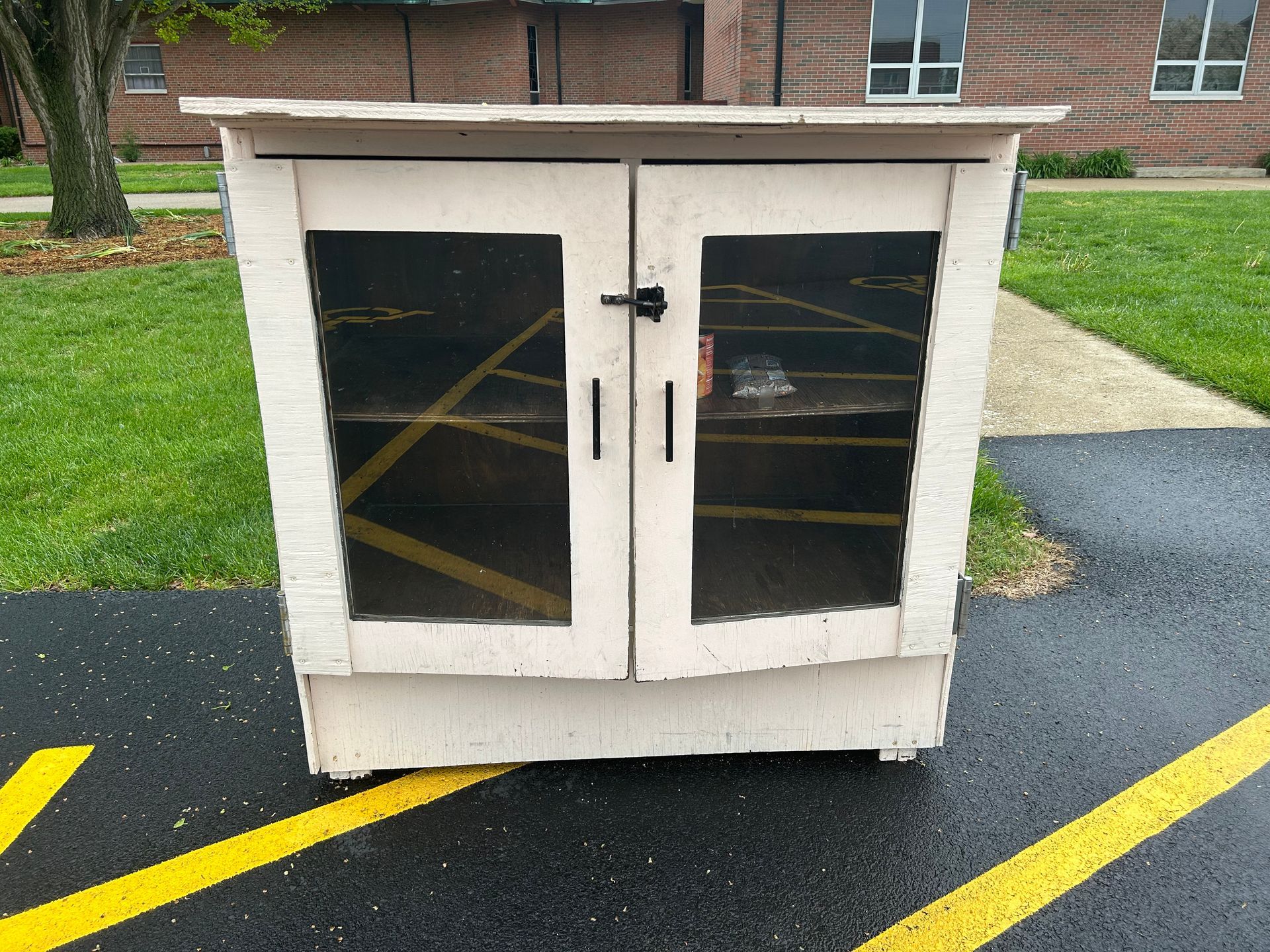 White Little Free Food Blessing Box on asphalt with yellow lines.