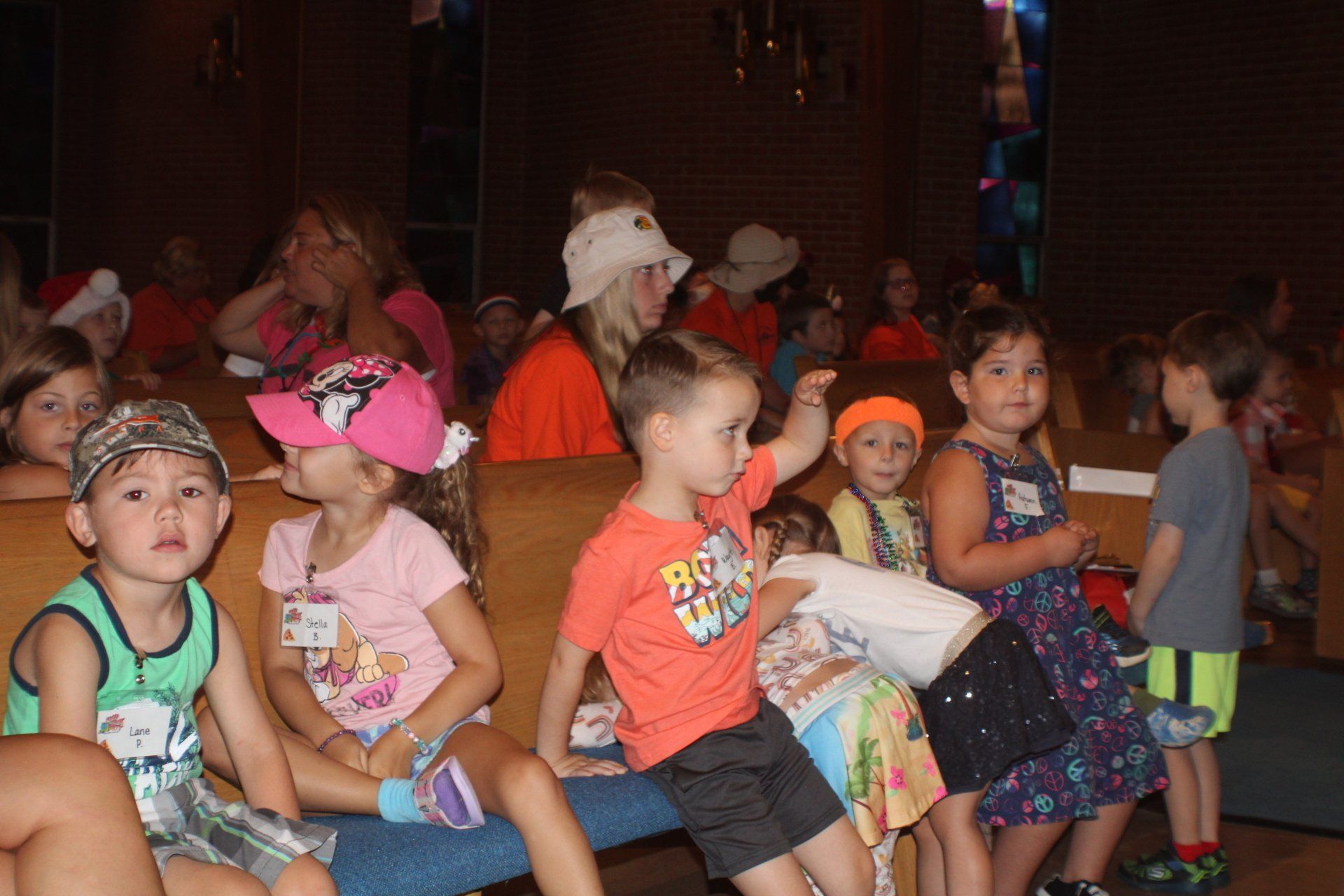 Children sitting on church pews, some looking at the camera, others with adults in the background.