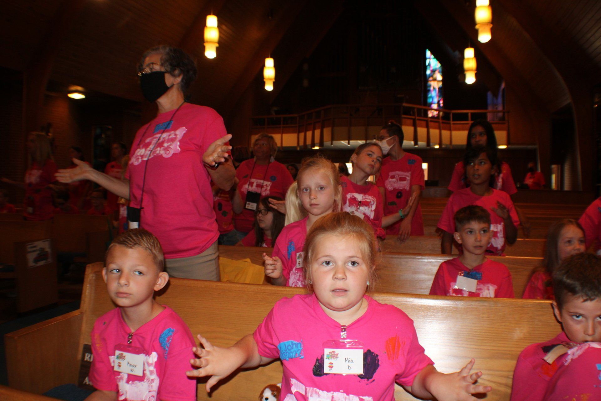 Children in pink shirts and a masked adult inside a church.