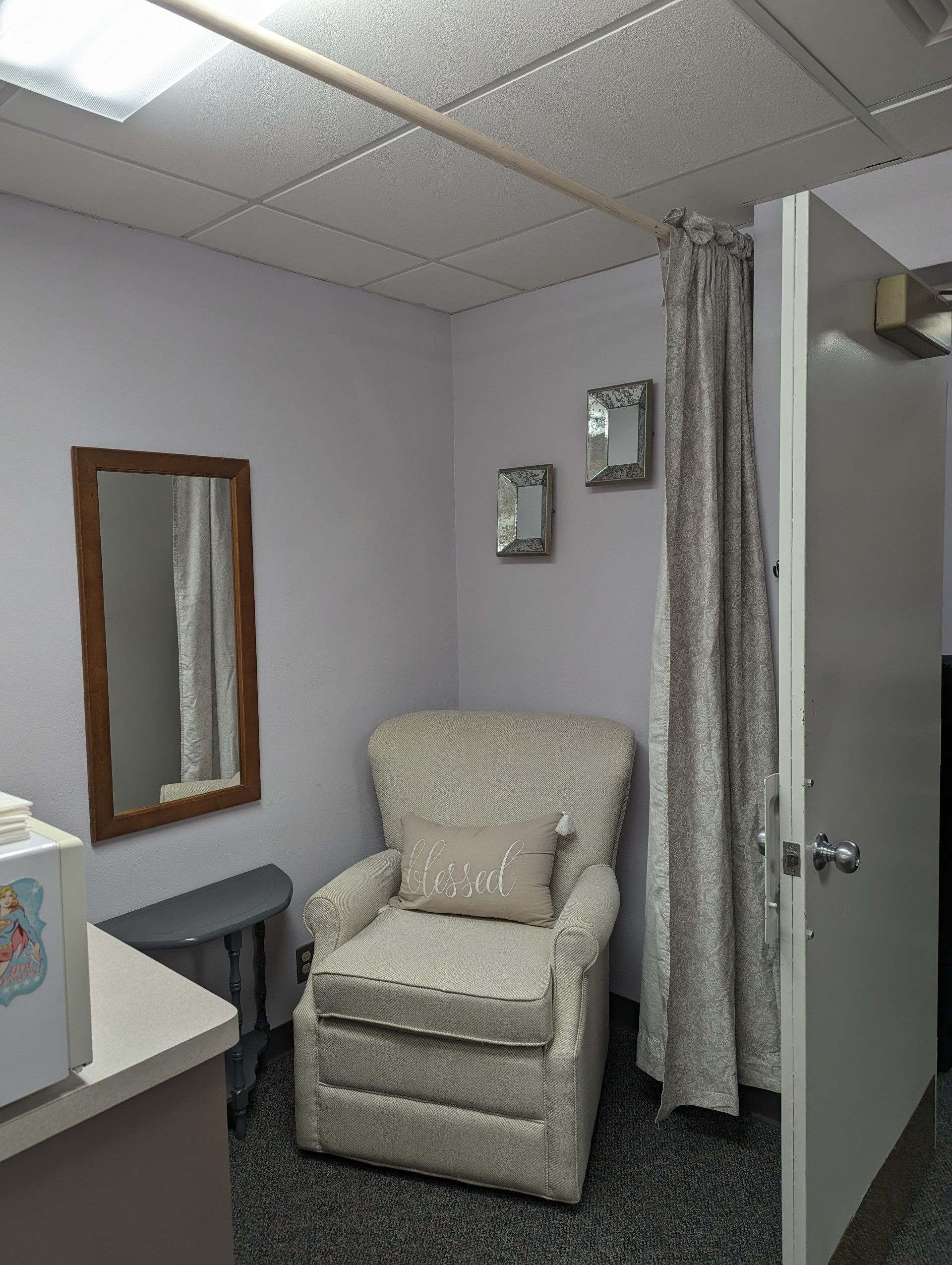 Small, lilac-walled room with patterned armchair, mirror, and curtain.