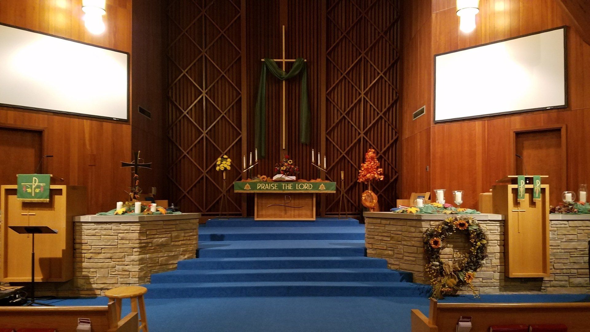 Interior view of a church sanctuary with a wooden altar, blue carpet, and two blank screens.