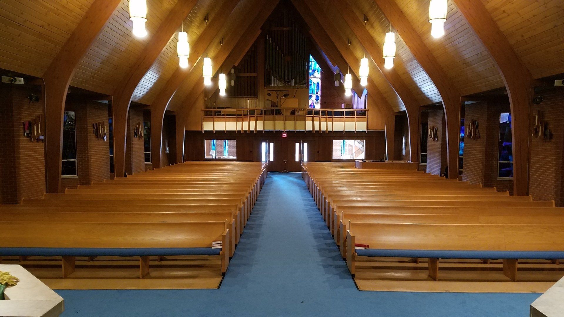 Interior view of a church with wooden pews and ceiling, blue carpet, and stained-glass windows.