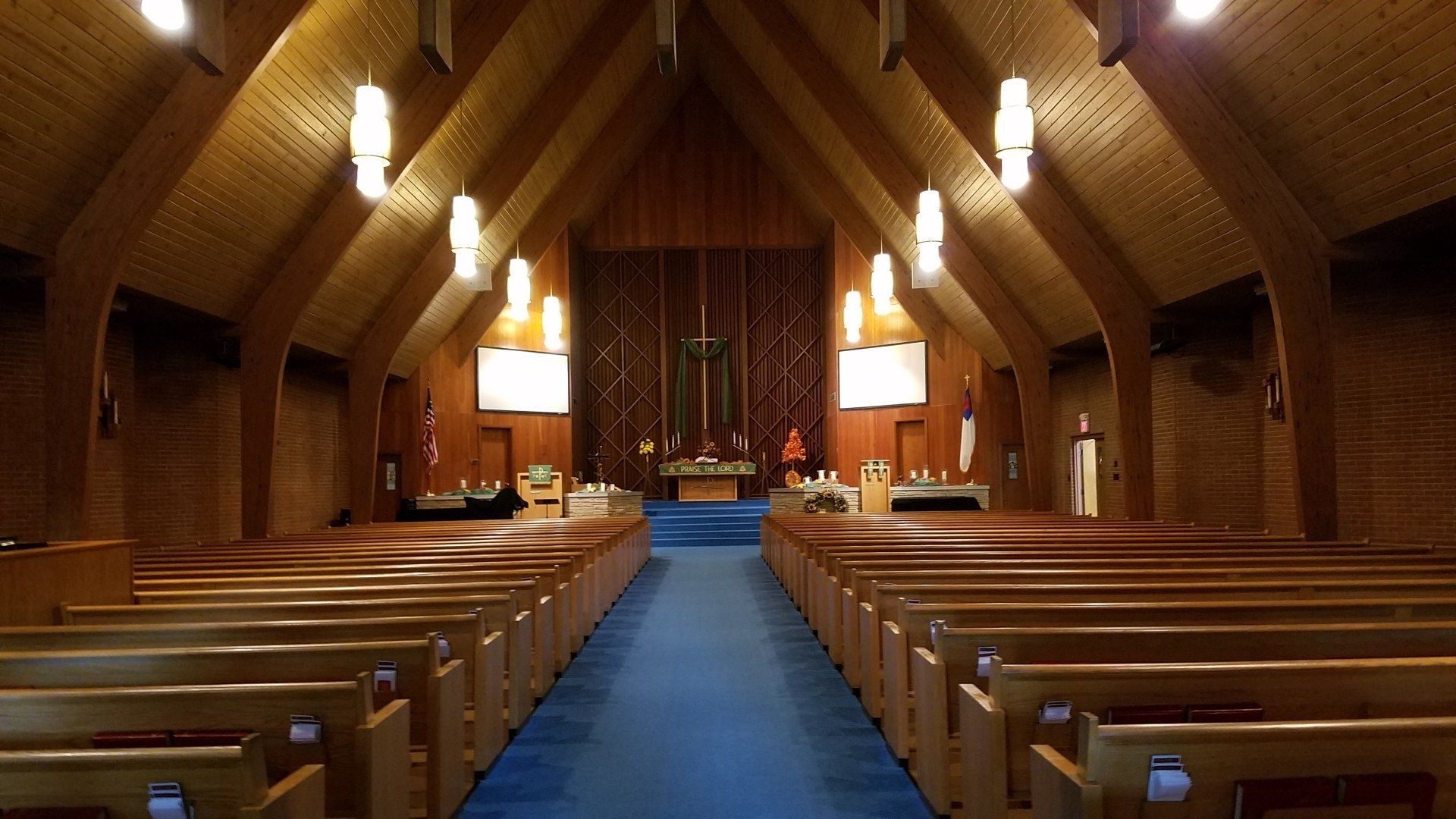 Interior of a church with wooden pews and ceiling, blue carpet, and a raised altar area.