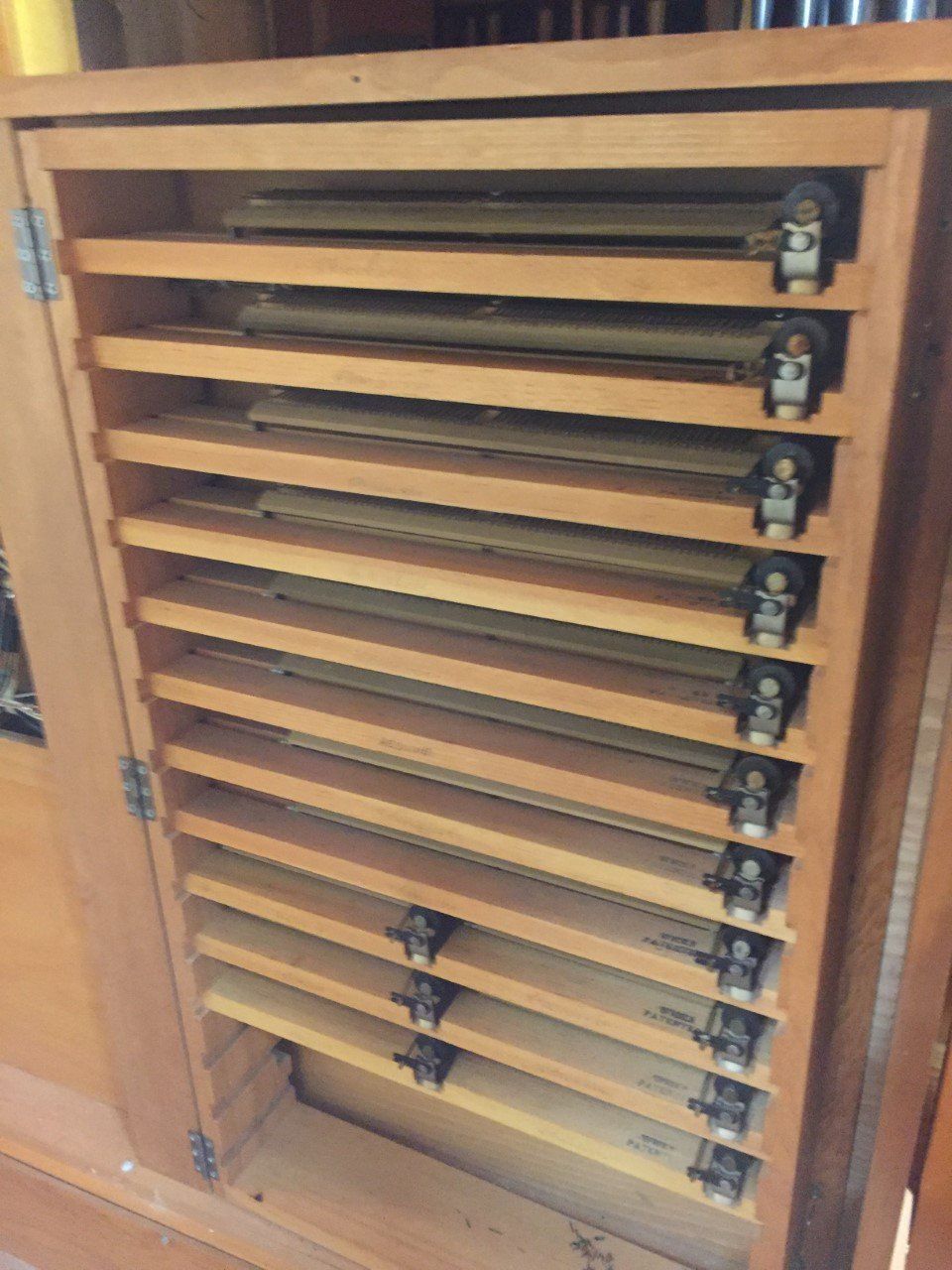 Wooden cabinet with horizontal shelves holding brass pipes, likely a pipe organ component.
