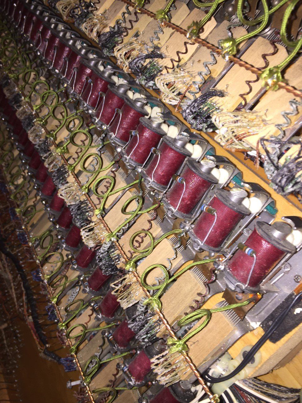 Close-up of a piano's internal mechanisms, showing red dampers, wires, and wooden parts in a row.