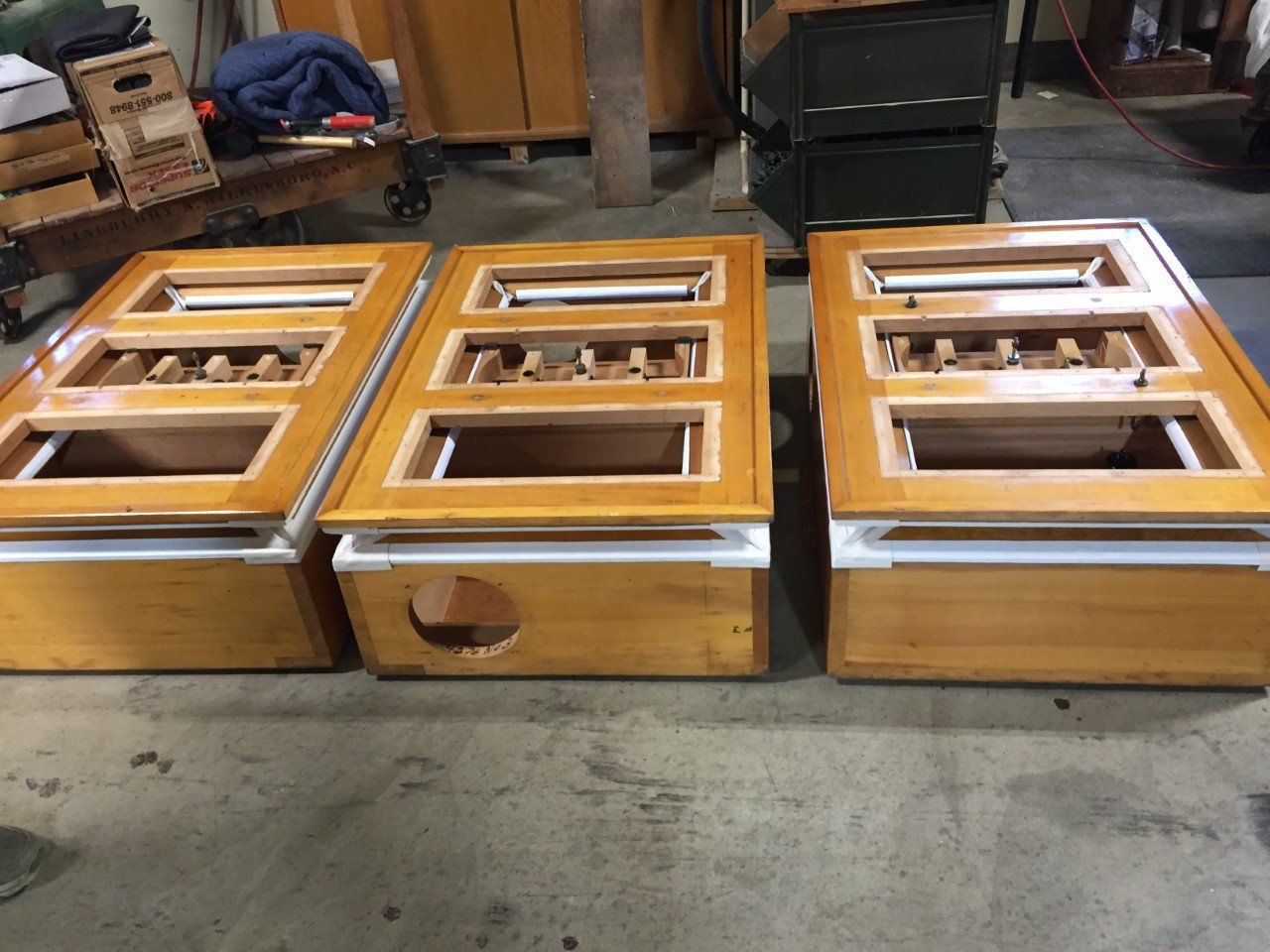 Three wooden boxes with light brown frames and white bases, side by side. Each has a rectangular opening.