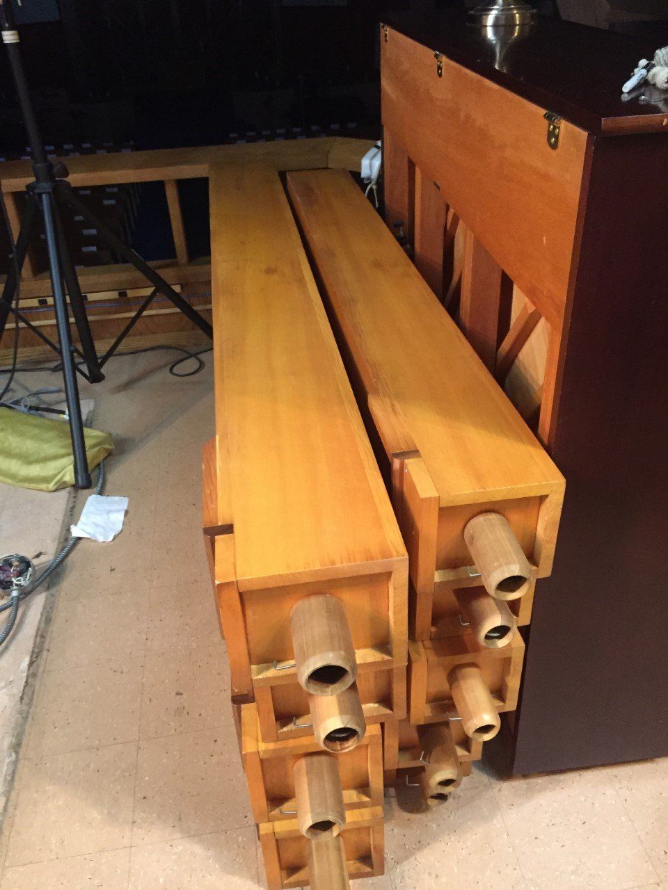 Wooden organ pipes, light brown, stacked near a dark wooden cabinet.