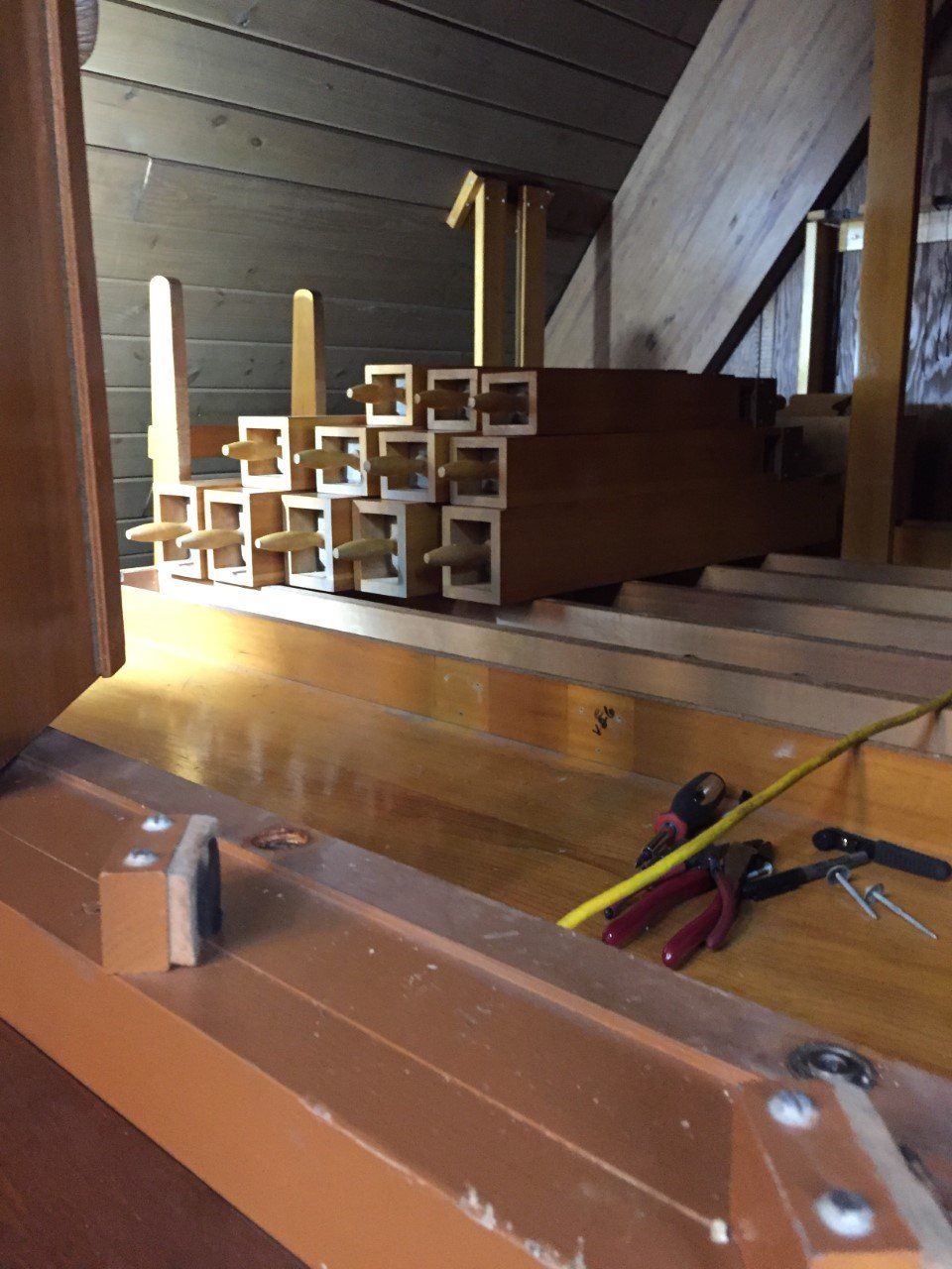 Interior view of an organ, showing wooden pipes and tools on a wooden surface.
