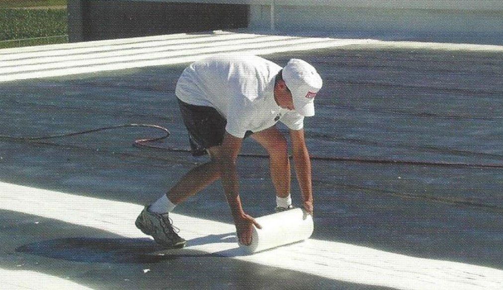 a man in a white shirt and black shorts is installing a roll of membrane coating on a surface