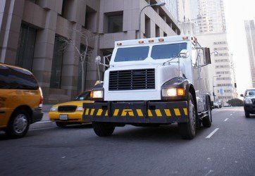 White armored truck on a city street, yellow taxi and other vehicles in the background.