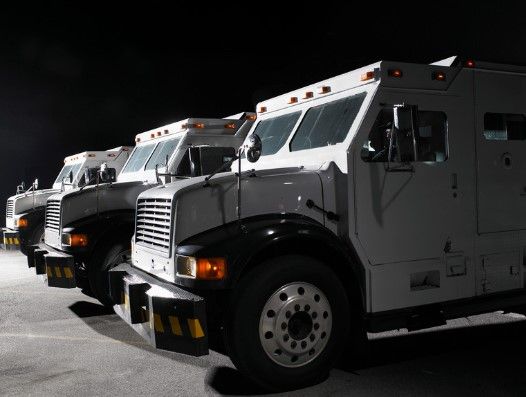Armored trucks, lined up in a row, with white exteriors and black detailing, under dark skies.