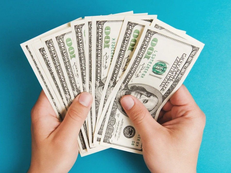 Hands holding a fan of United States $100 bills against a blue background.