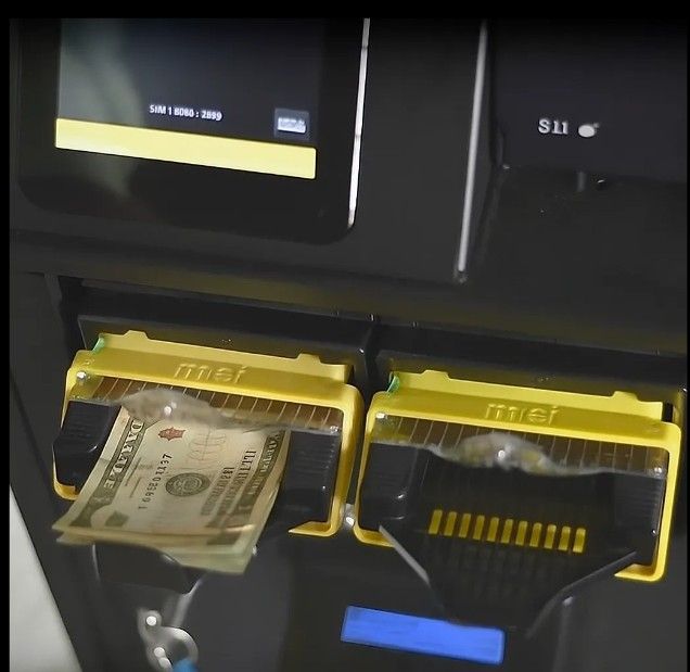 ATM with a twenty-dollar bill being dispensed into a yellow slot. The machine has a screen and another slot.