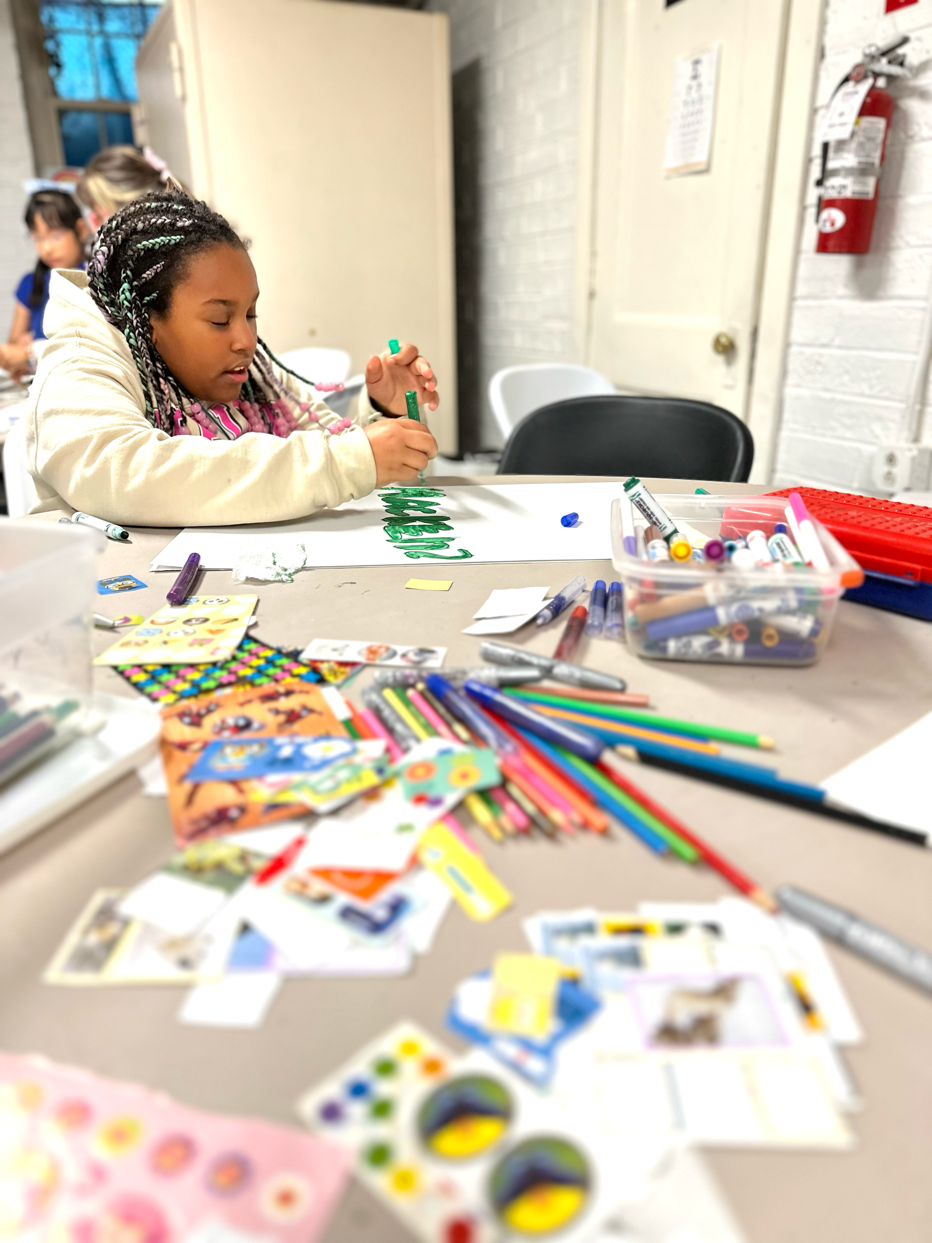 A little girl is sitting at a table with markers and stickers