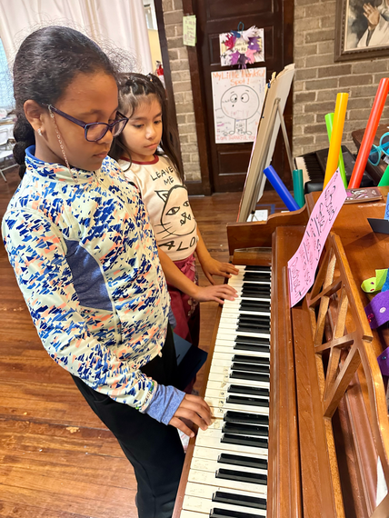 Two young girls are playing a piano in a room.