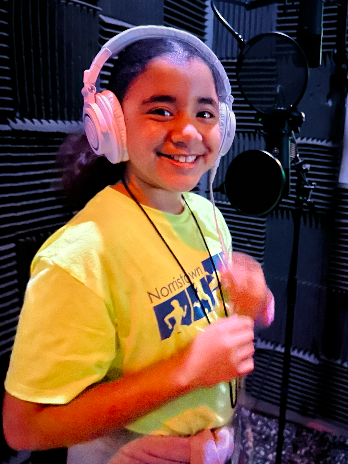 A young girl wearing headphones and a yellow shirt that says nomads on it