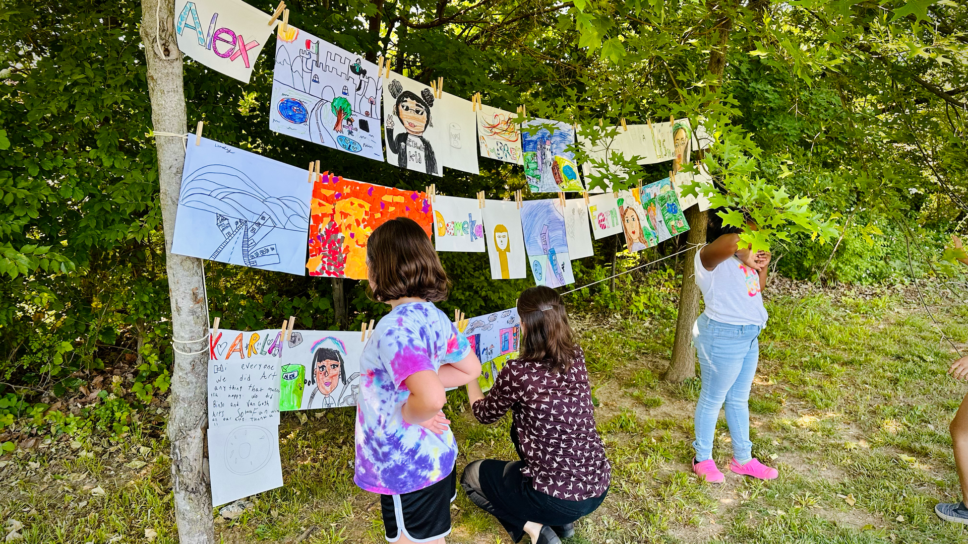 A group of children are looking at paintings hanging on a clothesline.