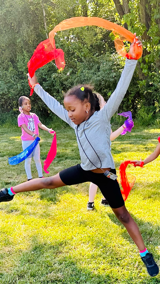 A young girl is jumping in the air while holding a colorful scarf.