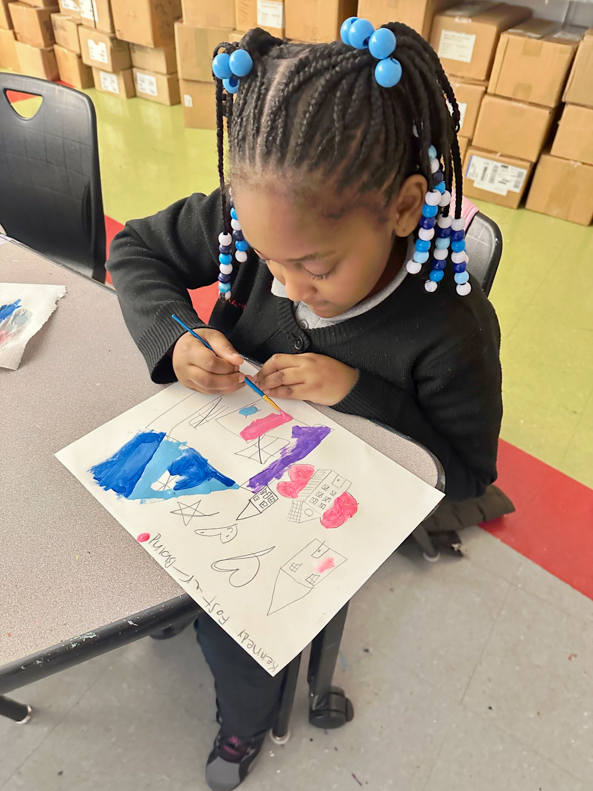 A little girl with braids is painting on a piece of paper