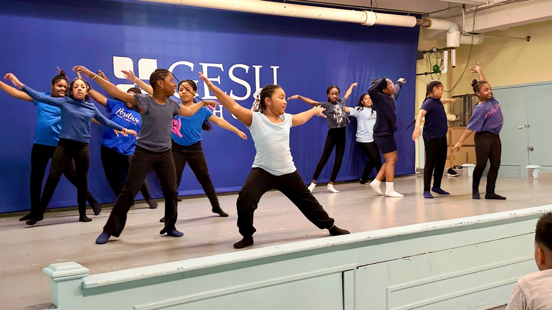 A group of young girls are dancing on a stage in front of a blue wall.