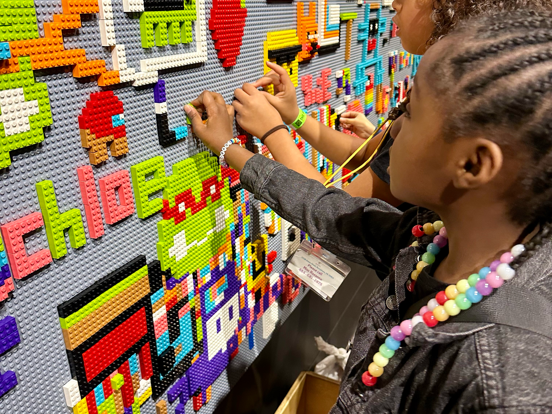 Two young girls are playing with lego blocks on a wall.