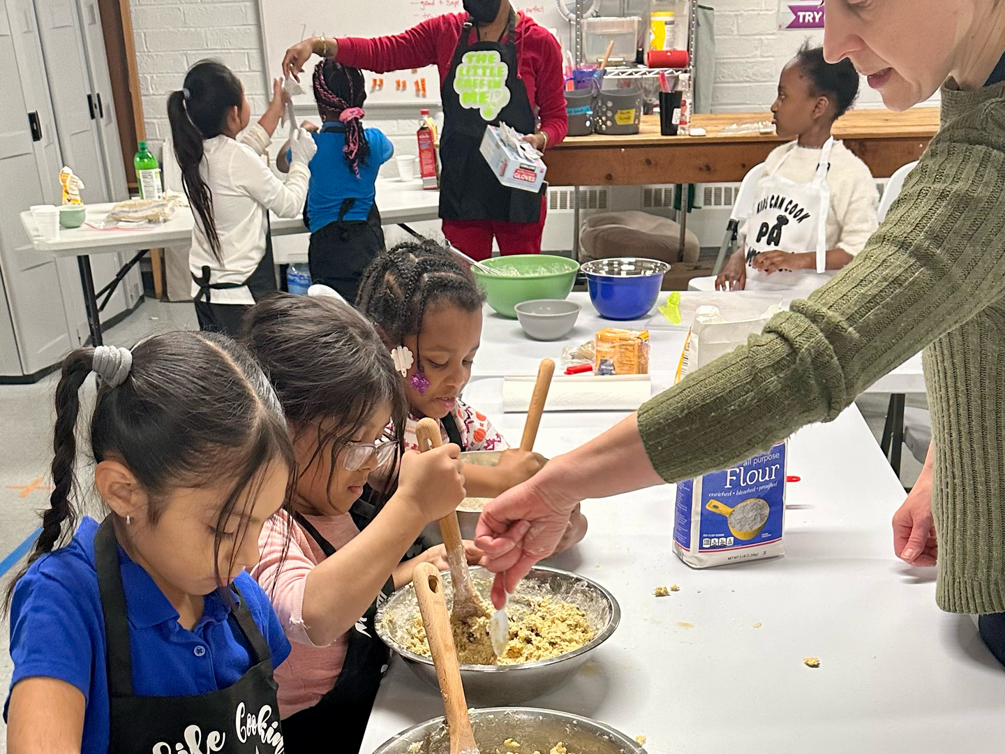 A woman is teaching a group of young girls how to cook.