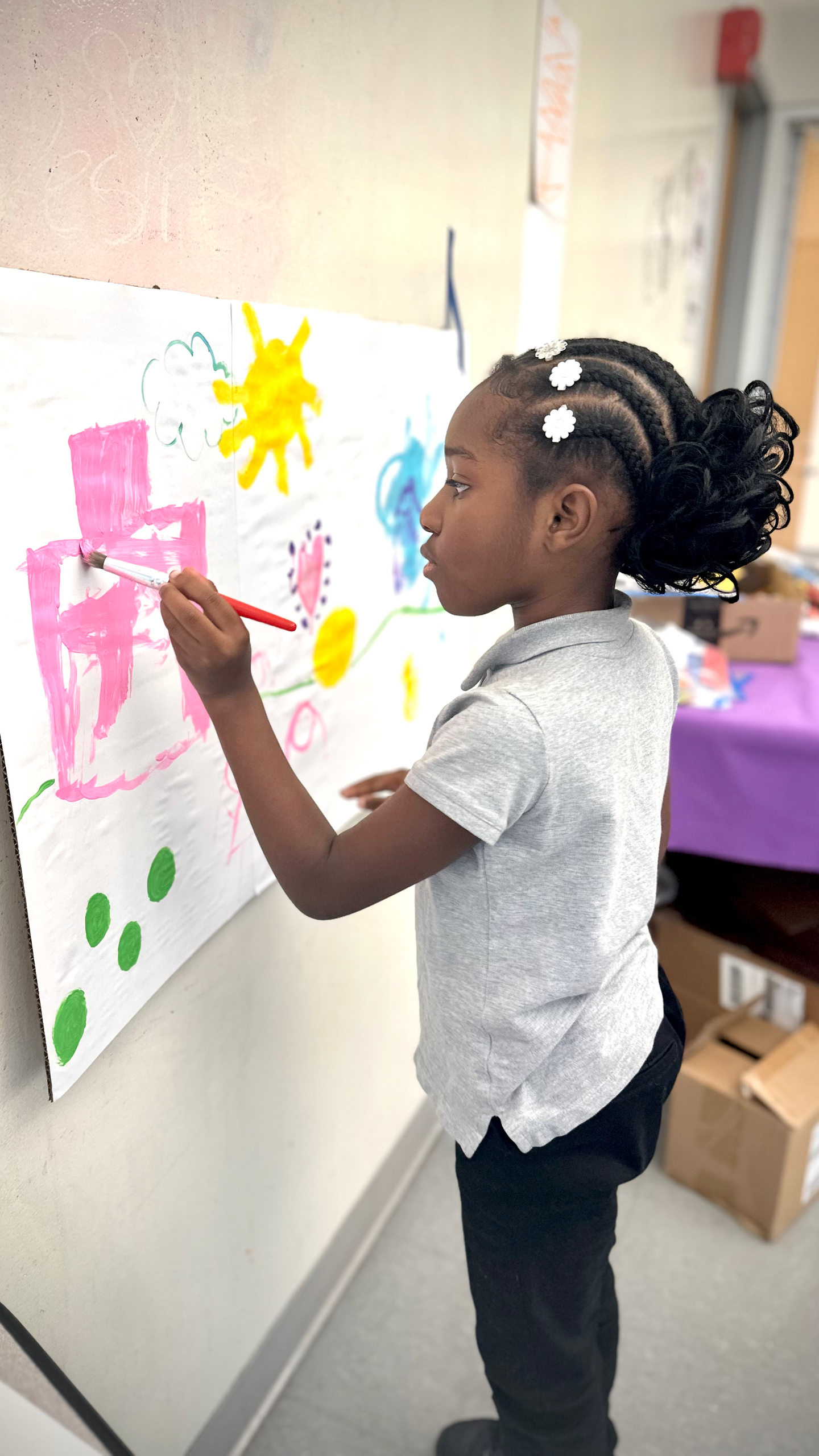 A little girl is painting on a white board with a brush.