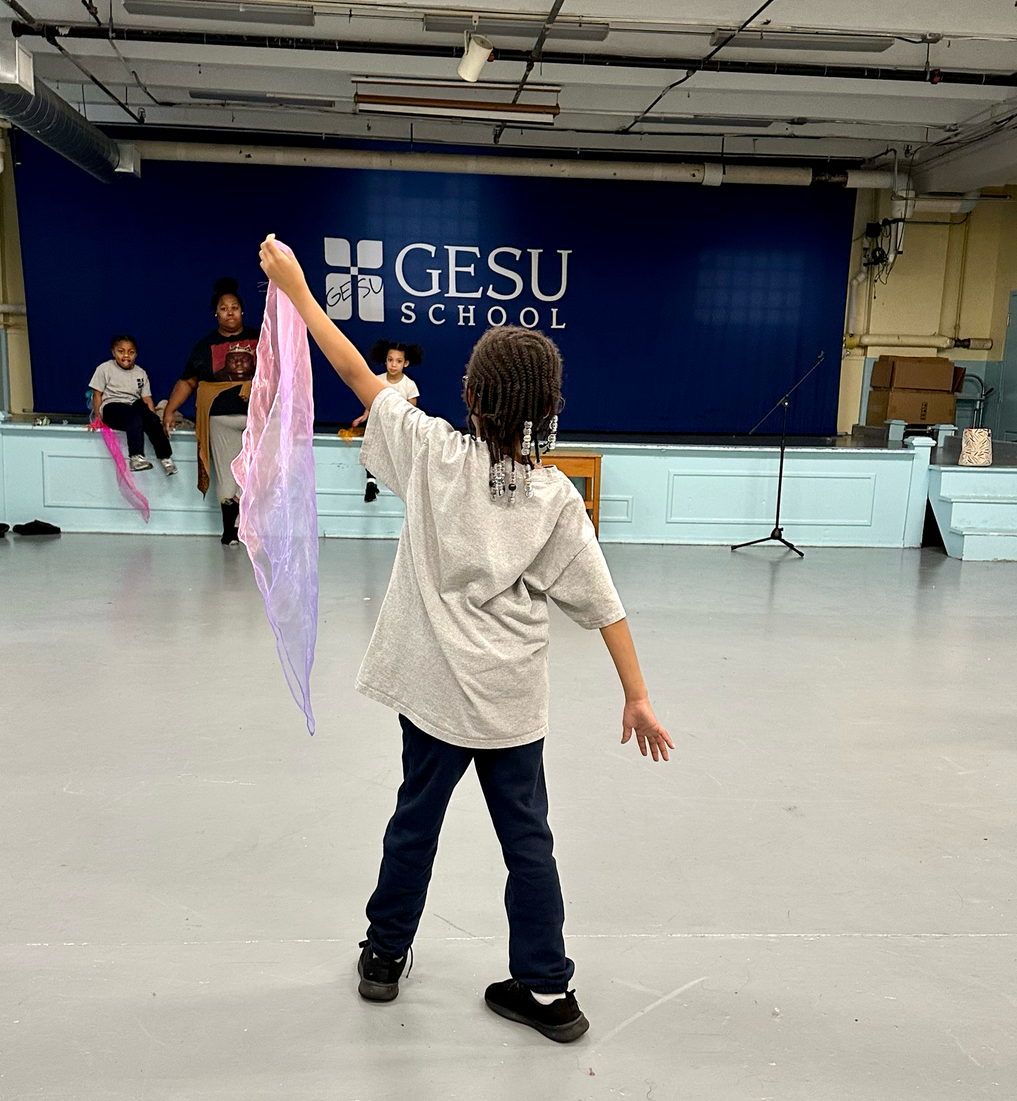 A girl is dancing in front of a sign that says gesu school