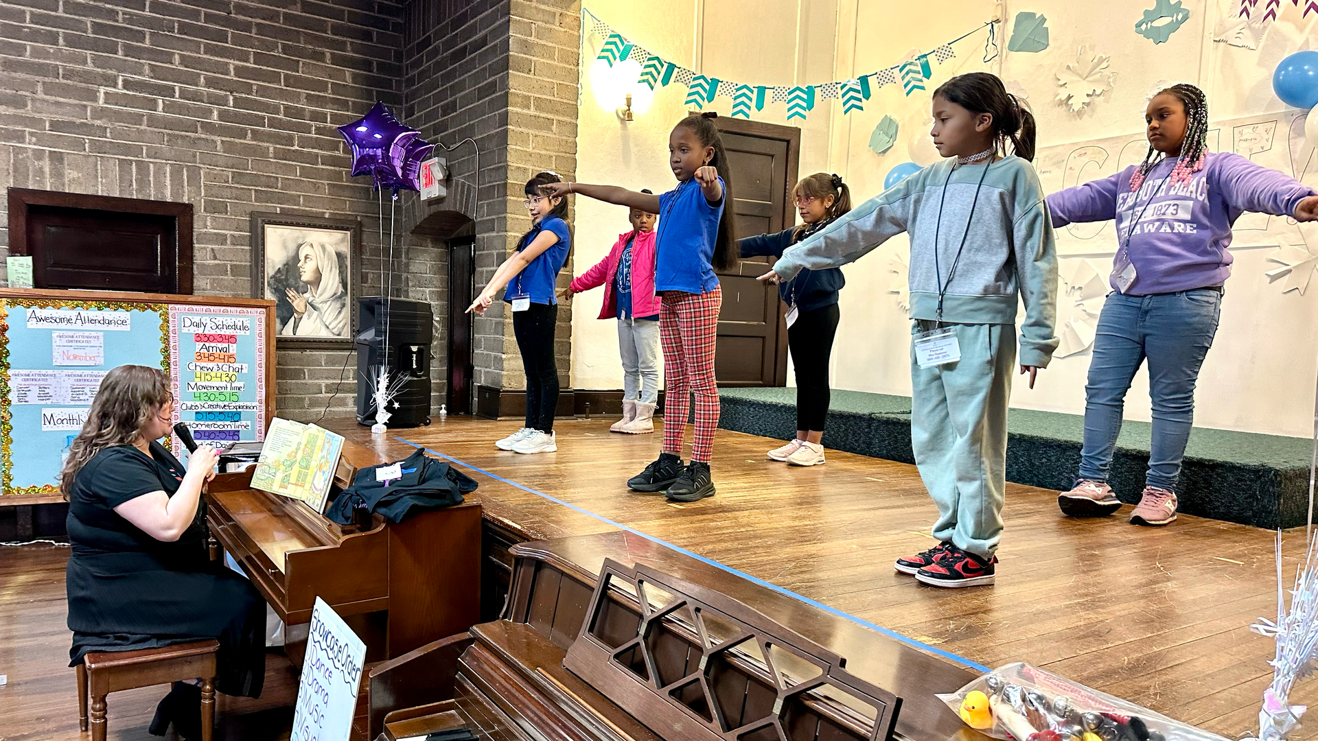 A woman is playing a piano while a group of children are dancing on a stage.