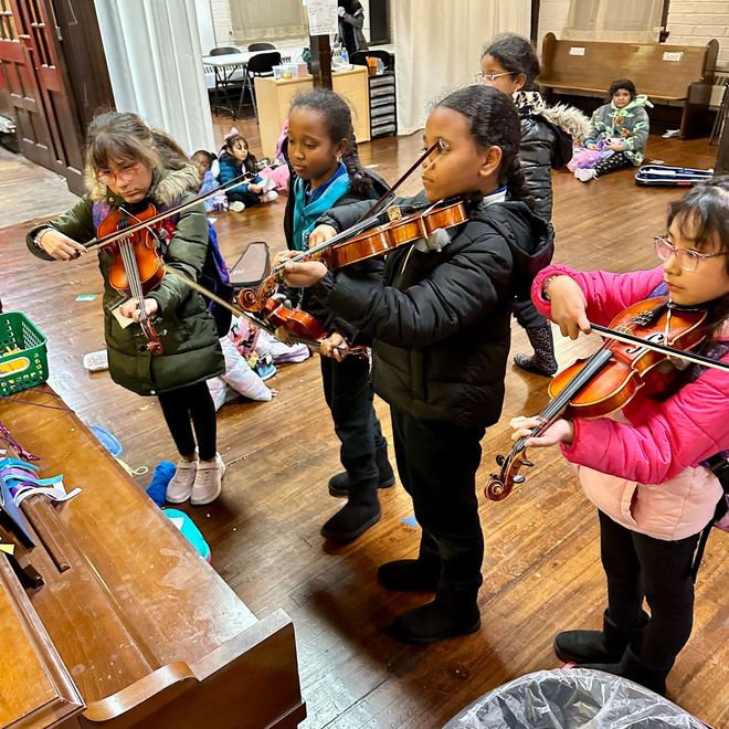 A group of young girls are playing violins in a room.