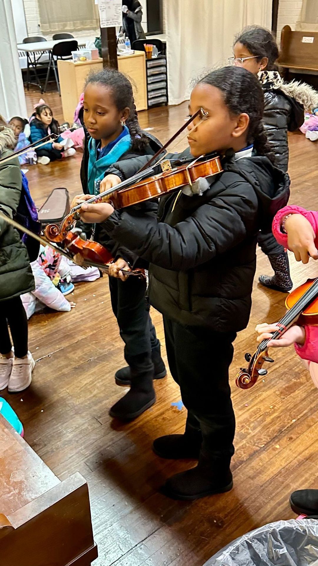 A group of children are playing violins in a room.