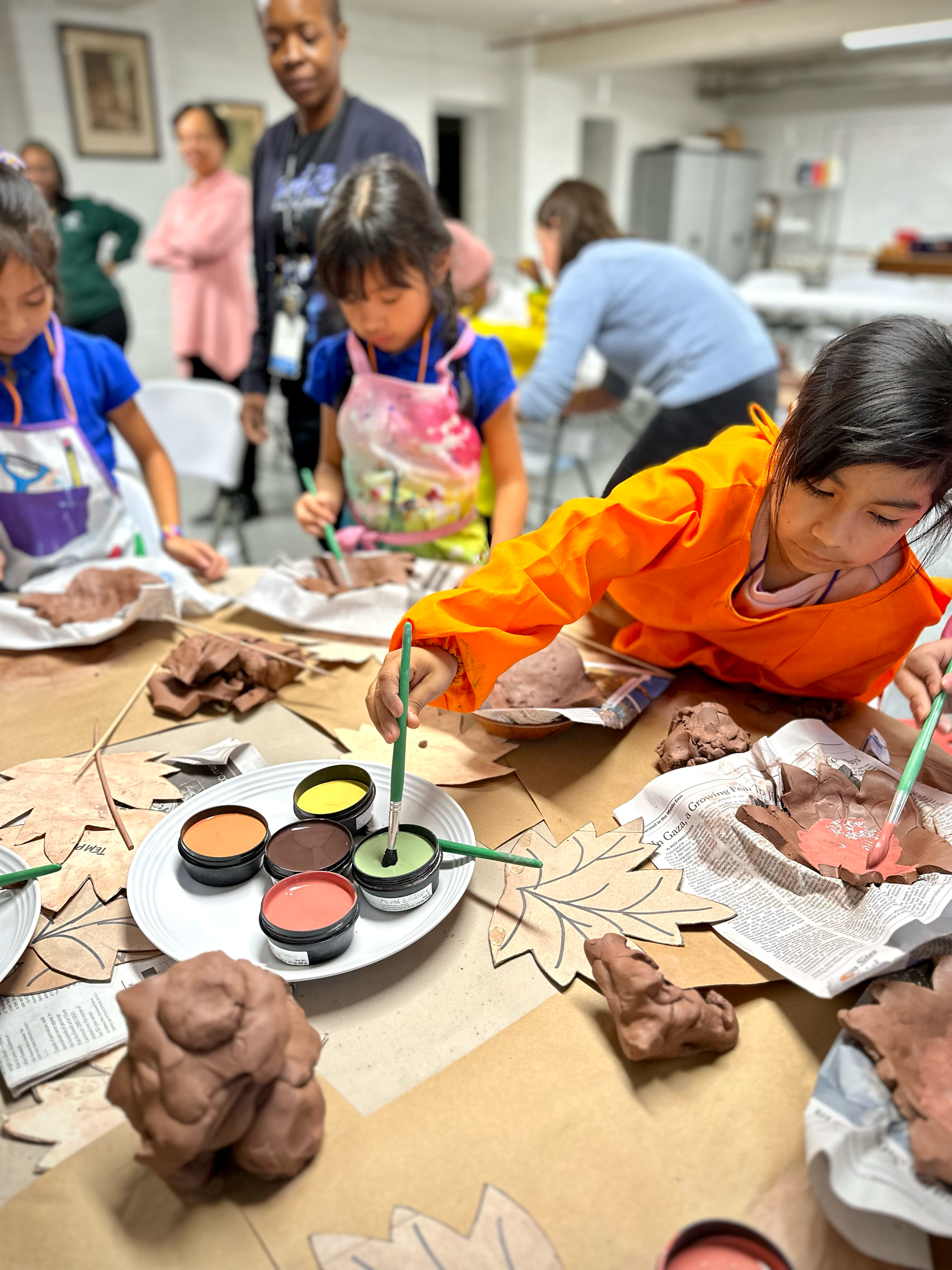 A group of children are sitting at a table painting clay.