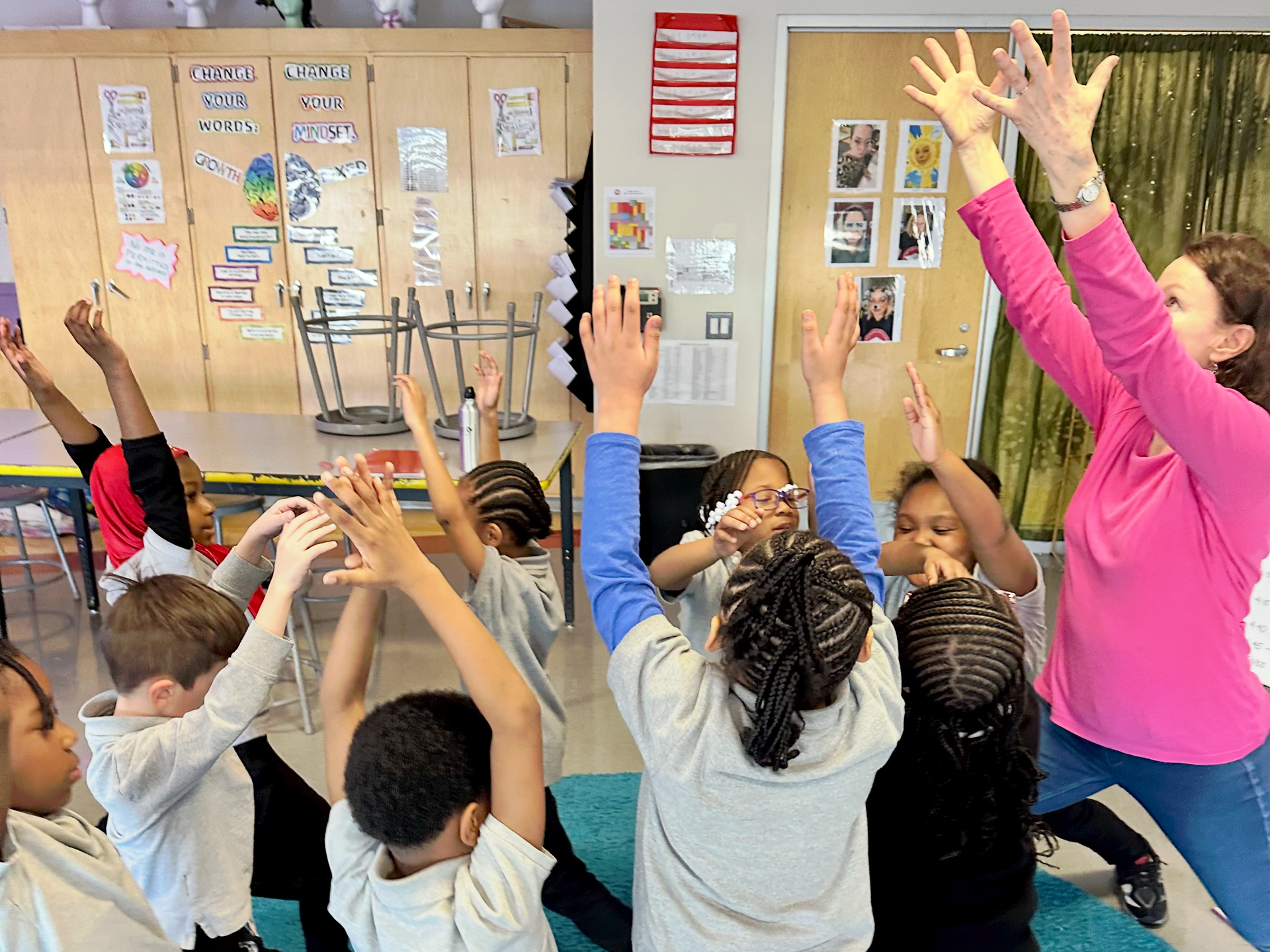 A woman in a pink shirt is teaching a group of children how to do yoga