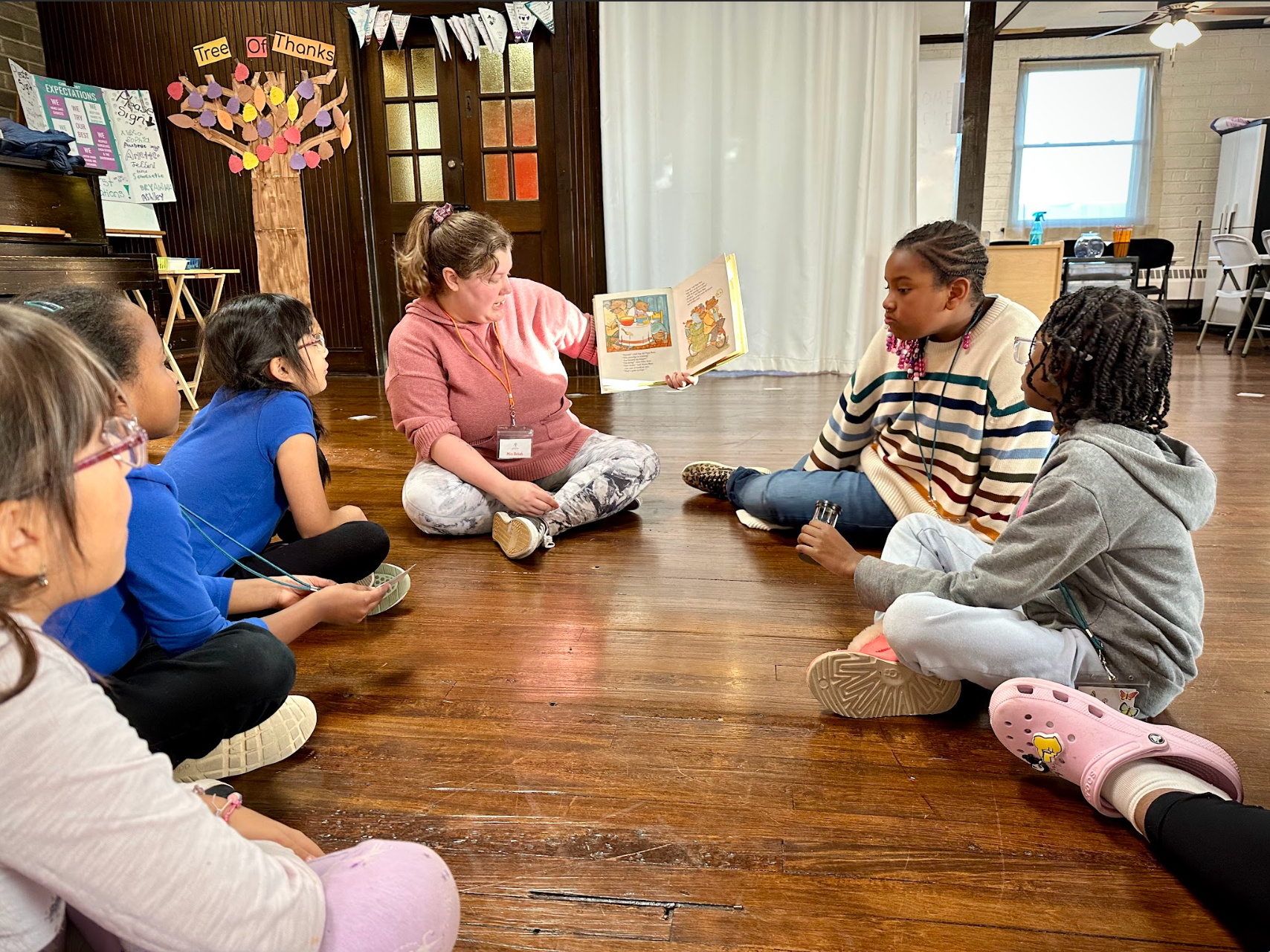 A woman is sitting on the floor reading a book to a group of children.