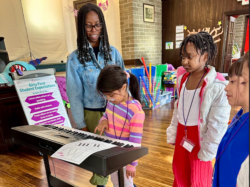 A woman is teaching a group of young girls how to play a keyboard.