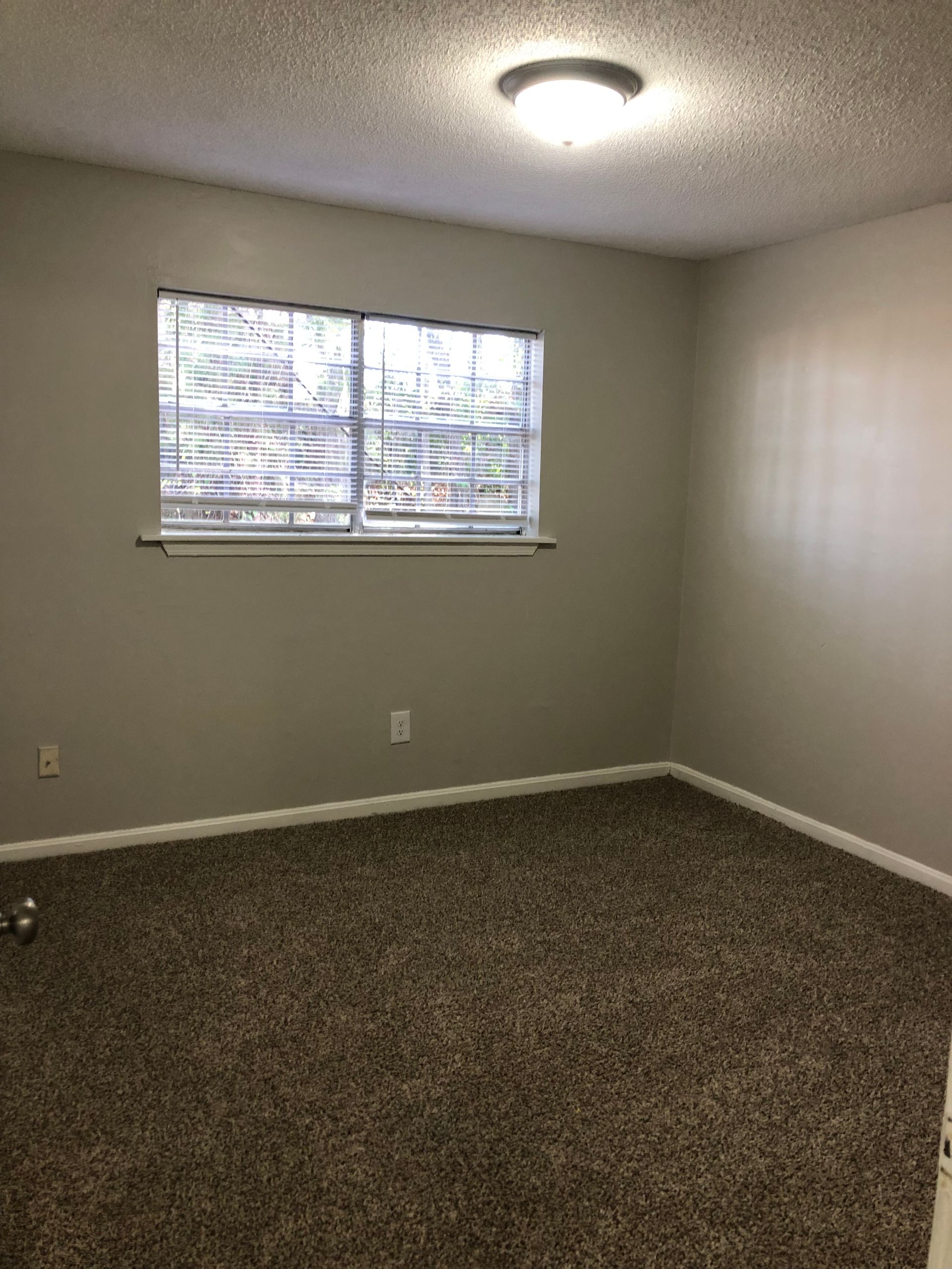 an empty bedroom with a window and blinds .