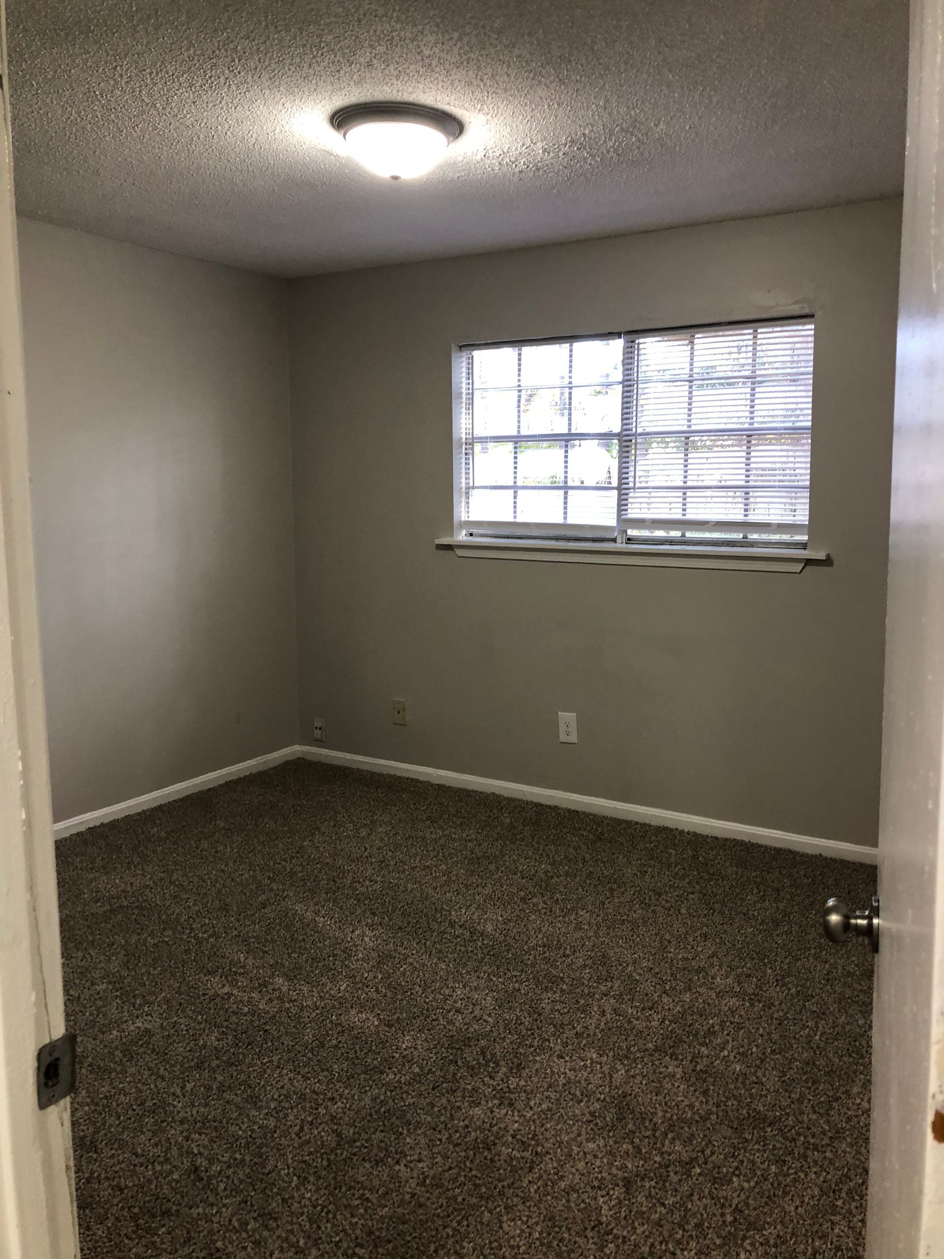 an empty bedroom with a window and a carpeted floor .
