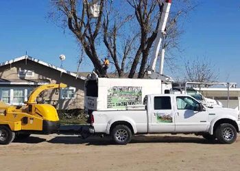 A white truck with a yellow machine attached to it is parked in front of a house.