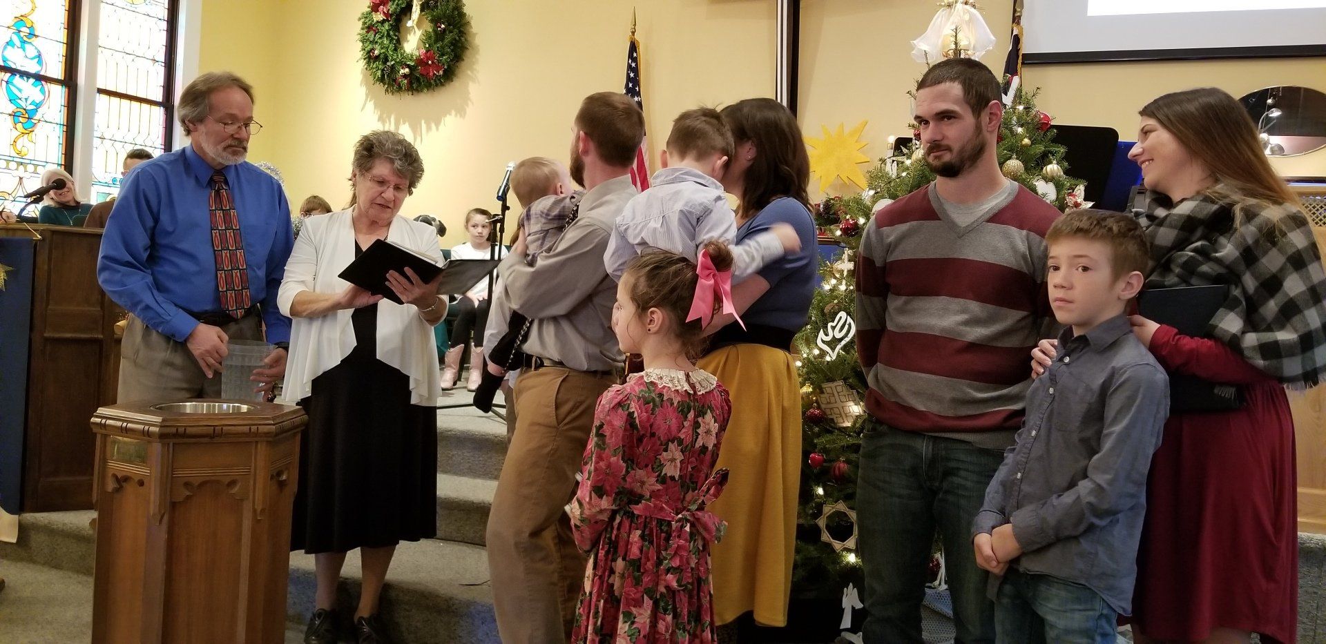 People gathered in a church for a baptism, Christmas decorations in the background.