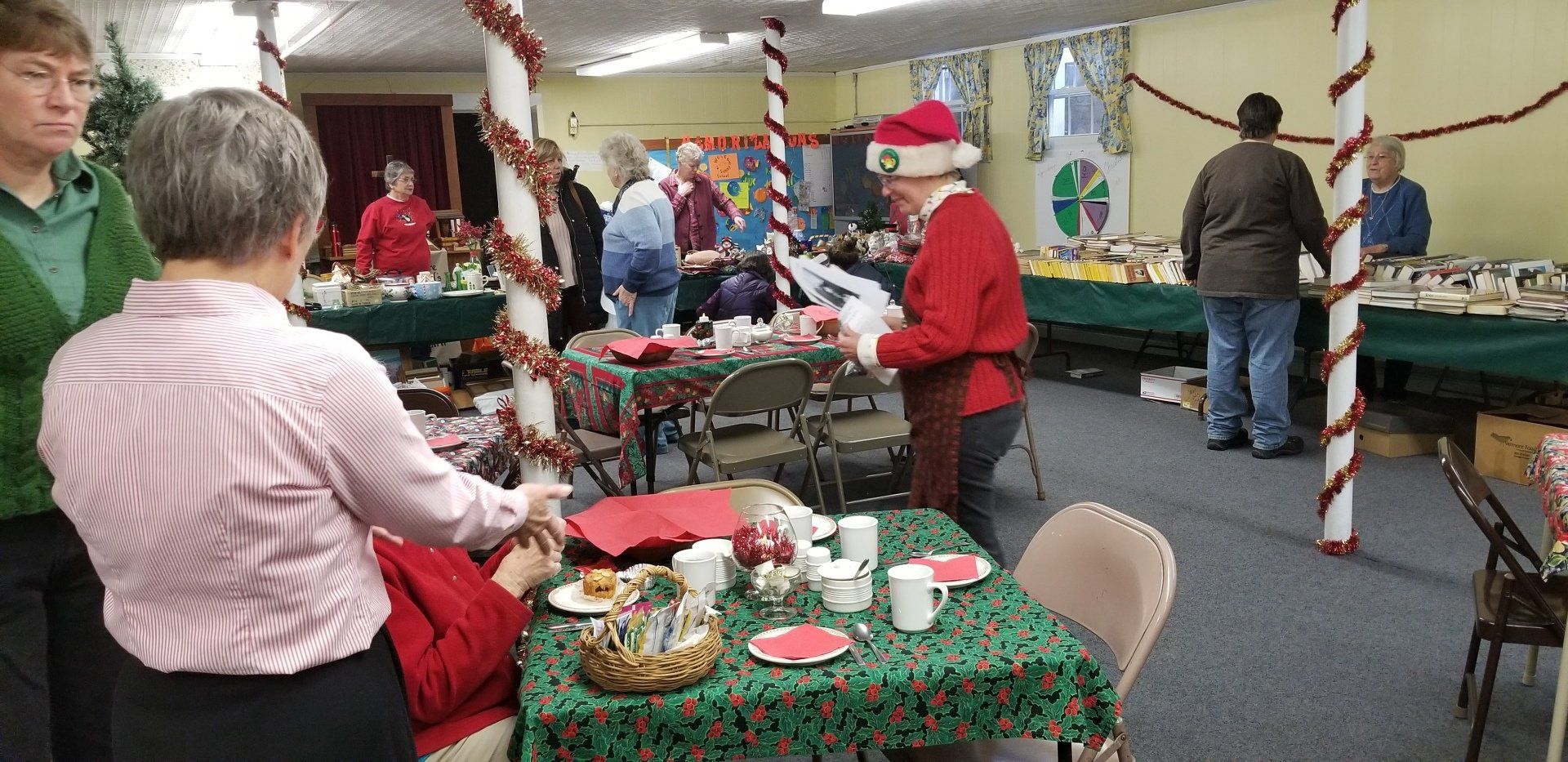 People in festive attire at an indoor holiday event, with tables, decorations, and refreshments.