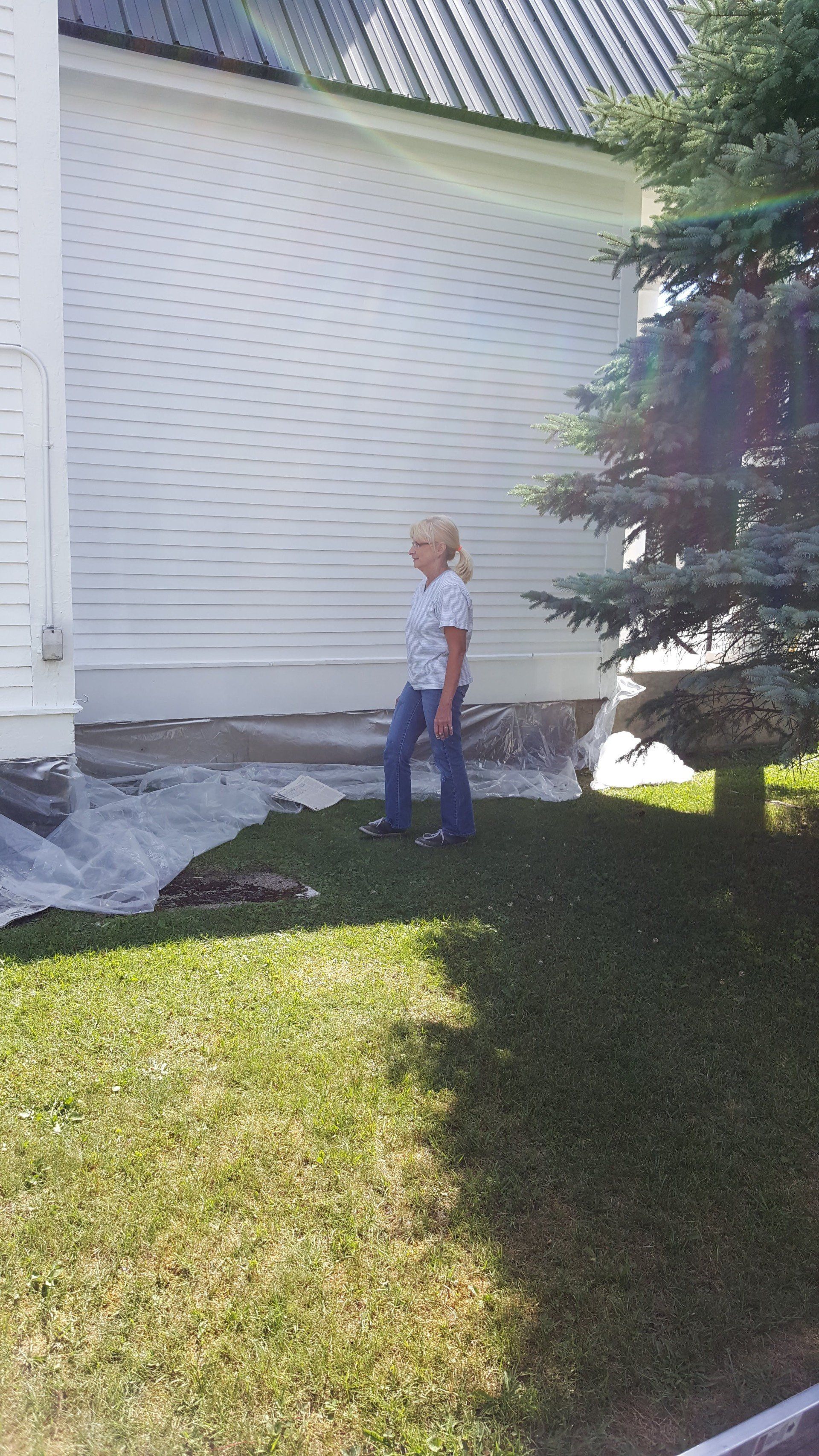 Woman walking on grass near a white building with a dark roof.