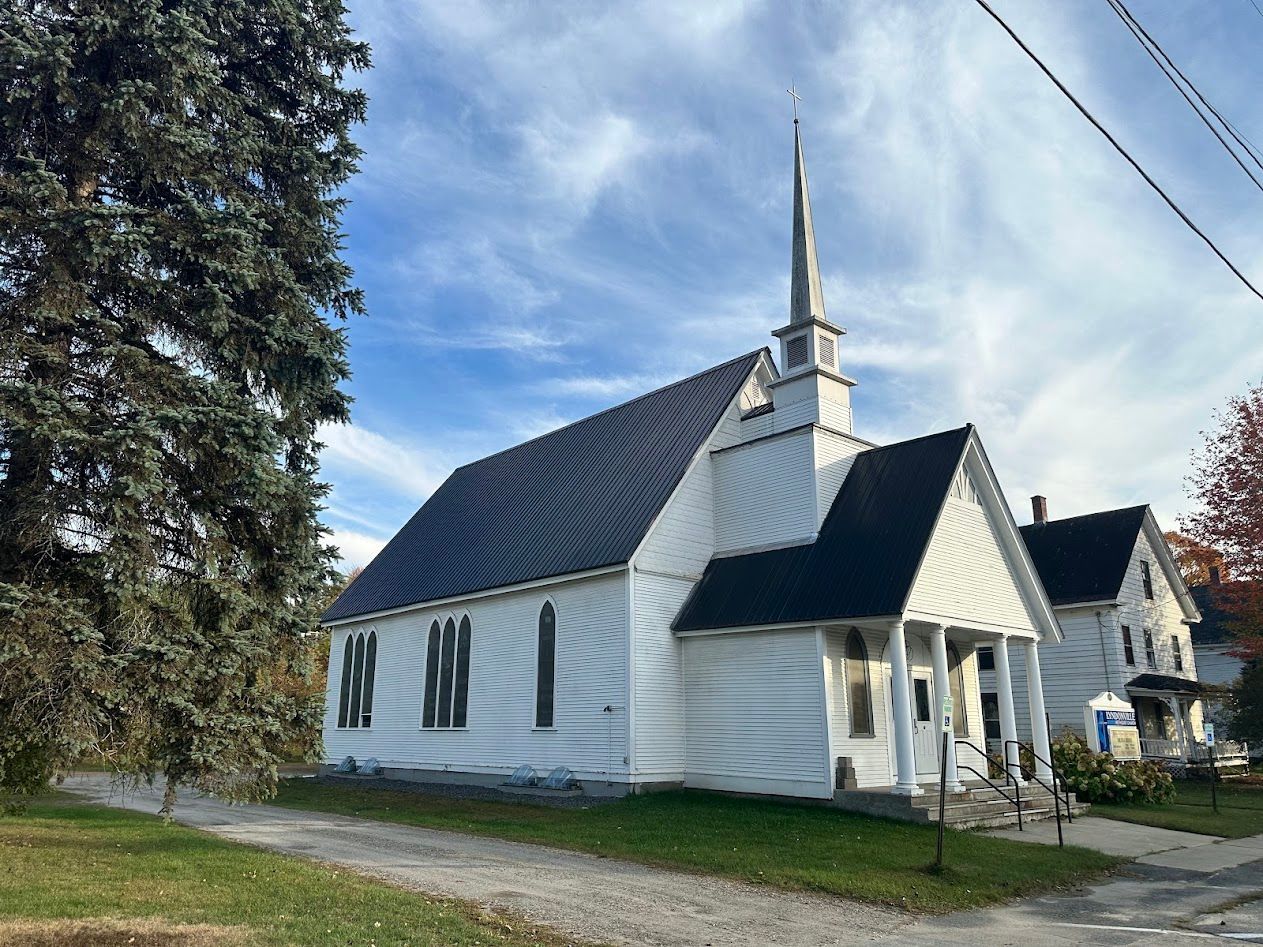 White church building with steeple, blue sky, and green grass.