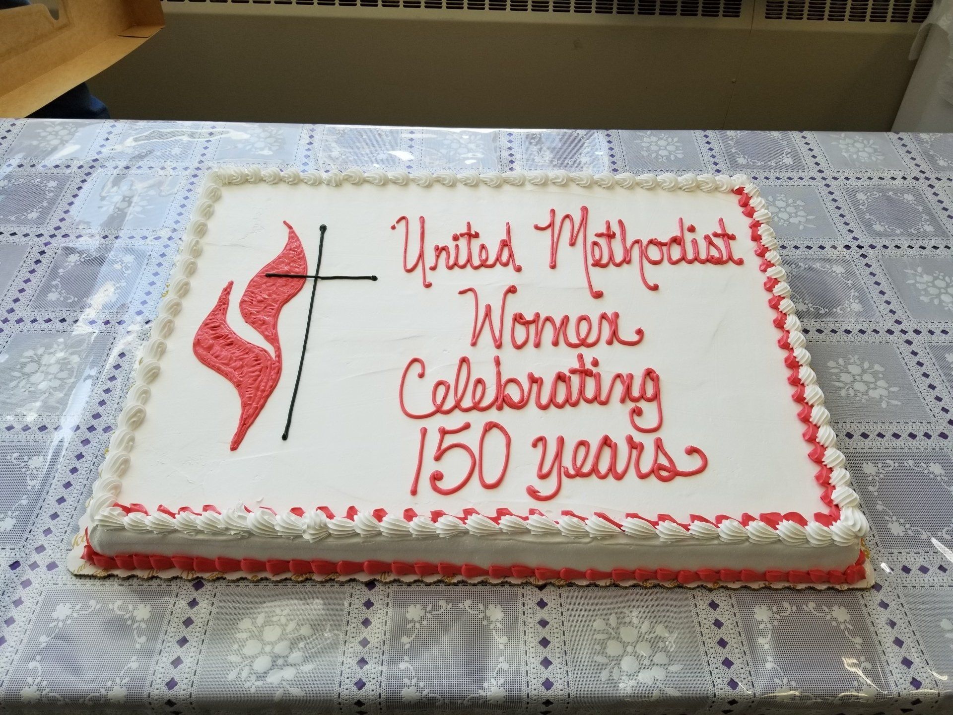 Cake celebrating United Methodist Women's 150th anniversary, red and white icing, flame and cross logo.
