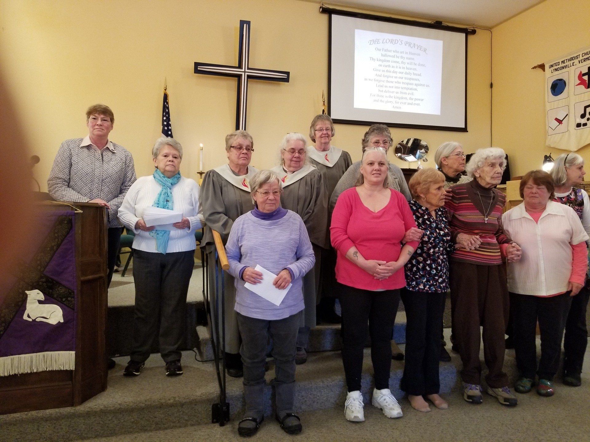 A group of people stand in a church, posing. A cross and projector screen are visible.