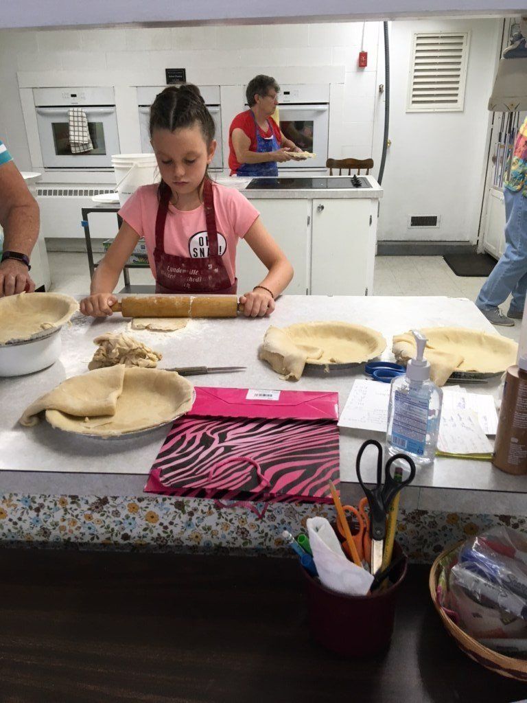 Girl rolling out dough in a kitchen with pie crusts. An older woman is in the background.